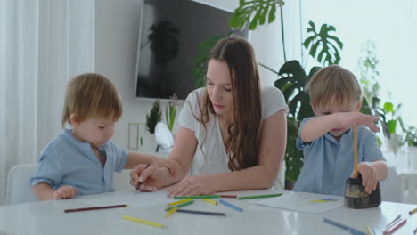 Mutter-Hilft-Zwei-Söhnen-Im-Alter-Von-2-Und-4-Jahren-Bei-Den-Hausaufgaben-Im-Vorschulalter,-Um-Ein-Bild-Mit-Bleistiften-Zu-Zeichnen