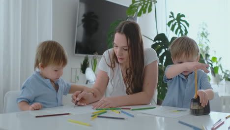 Mom-helps-two-sons-of-2-and-4-years-old-to-do-preschool-homework-to-draw-a-picture-with-pencils