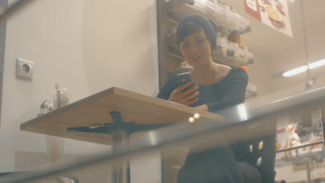 Cheerful-woman-in-cafe-communicating-online-on-cellphone