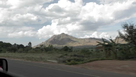 highway travel in malawi africa with farms, mountains, and vehicles seen, view from vehicle advancing