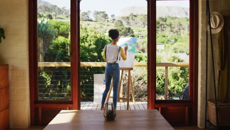 biracial woman painting on canvas in the balcony at home