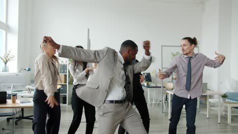 carefree men and women in formal clothing dancing at business party in coworking area