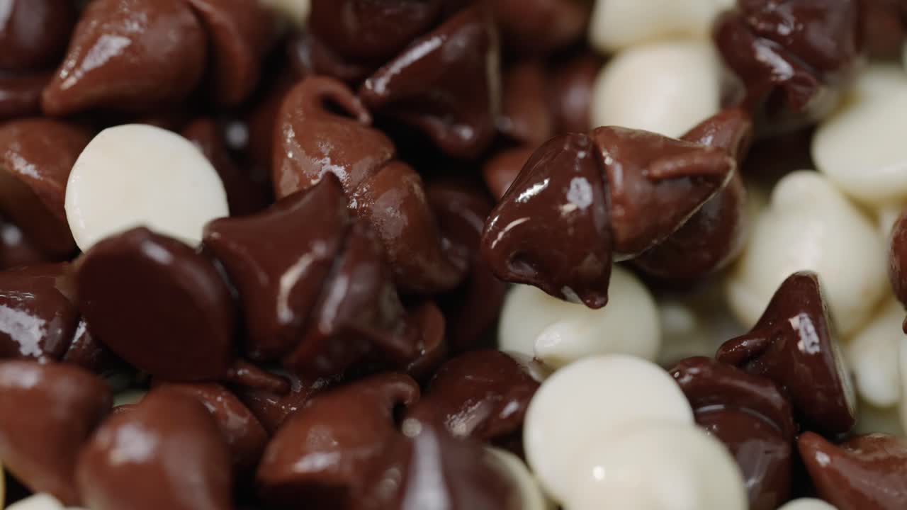 pila de chispas de chocolate derretidas calientes de múltiples variedades que brillan en macro de luz de cerca barrido de luz de 4k y pan a la derecha, blanco oscuro y chocolate con leche