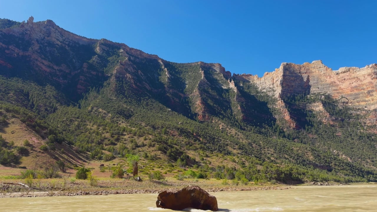 Scogliere illuminate dal sole e creste montuose si affacciano sull'ampio paesaggio della valle di Yampa, un ampio sfondo panoramico, esperienza di packrafting nell'entroterra.