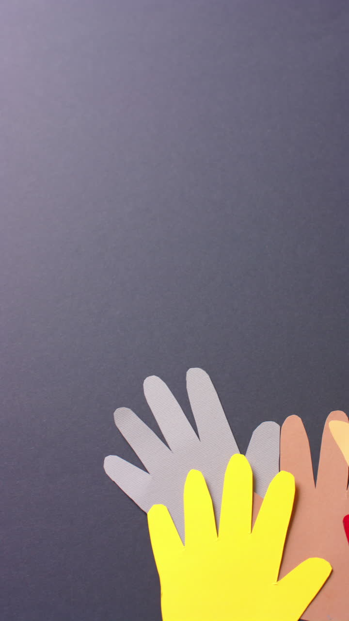 Vertical video of hands together made of colourful paper on gray background with copy space