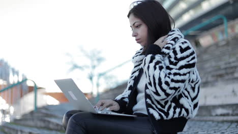 concentrated young woman sitting outdoor with laptop on knees