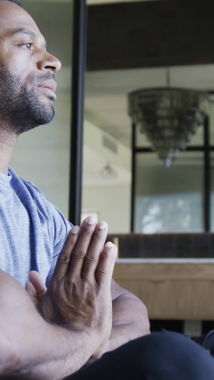 Vertical video: Breathing, man opening eyes, holding pressed hands in studio, gray tee, copy space