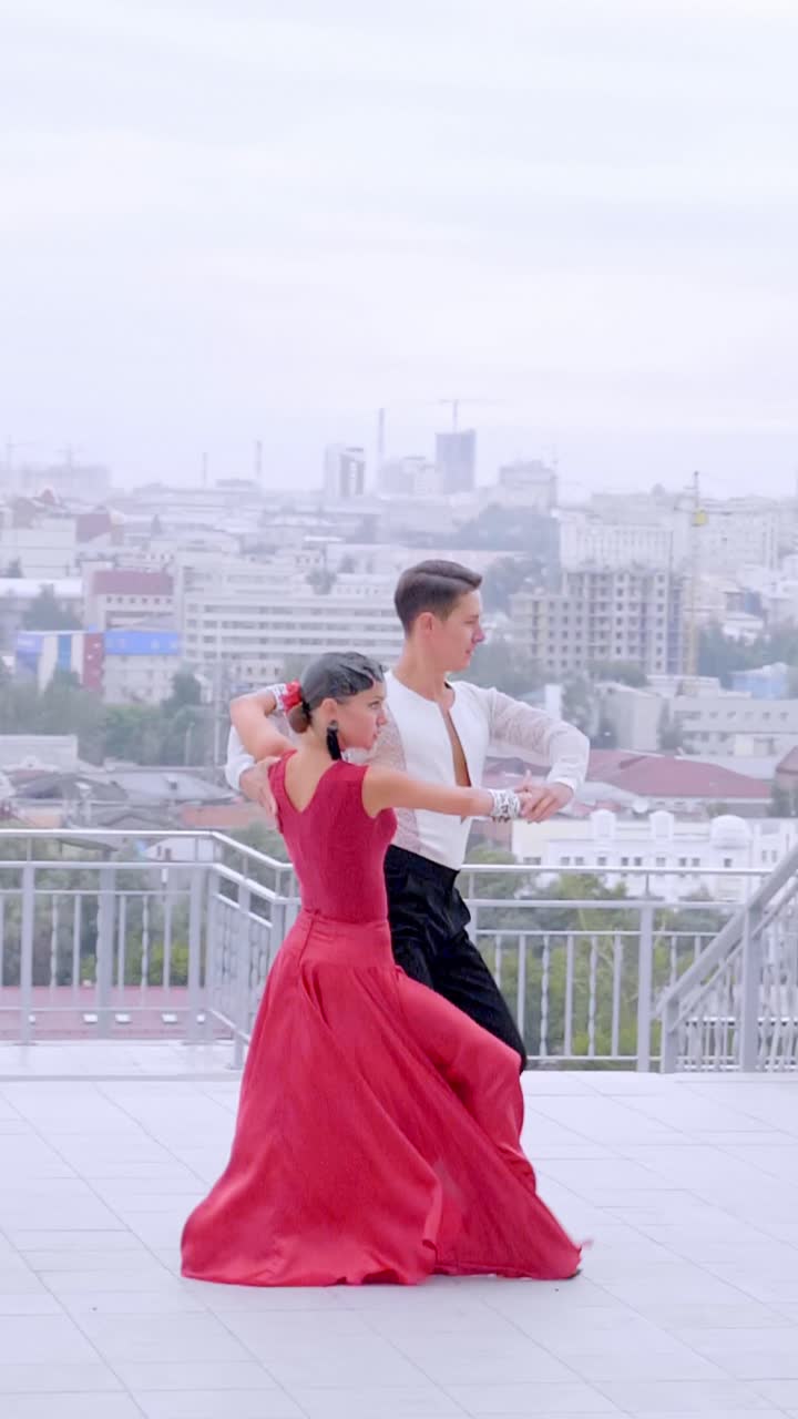 Elegant couple dancing in red dress and black suit against a city skyline backdrop