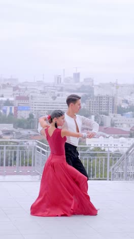 elegant couple dancing in red dress and black suit against a city skyline backdrop