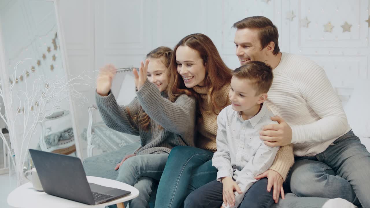 padres felices y niños agitando las manos frente a la pantalla de la computadora.