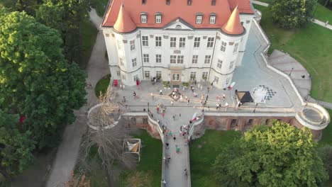 People-dancing-by-Lesnica-castle-on-early-sunny-morning,-Wroclaw-city,-Poland,-aerial-crane-shot