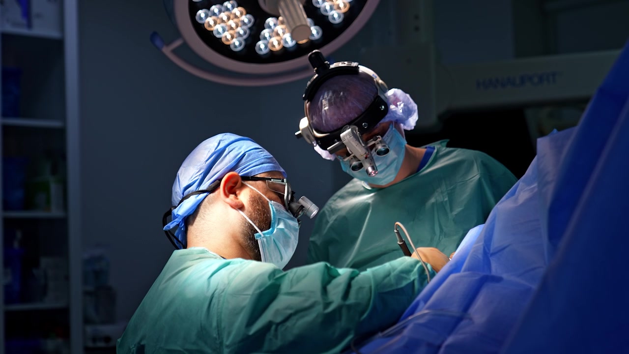 Due chirurghi uomini con occhiali ingranditori chirurgici usano uno strumento elettrico che produce fumo durante l'utilizzo. I medici eseguono un intervento per un trauma.