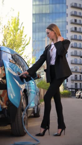 close-up of woman charging electric blue car at station. vertical video