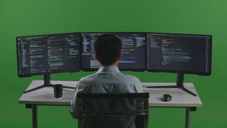 back view of asian man developer using computer to write code with multiple screens in green screen studio