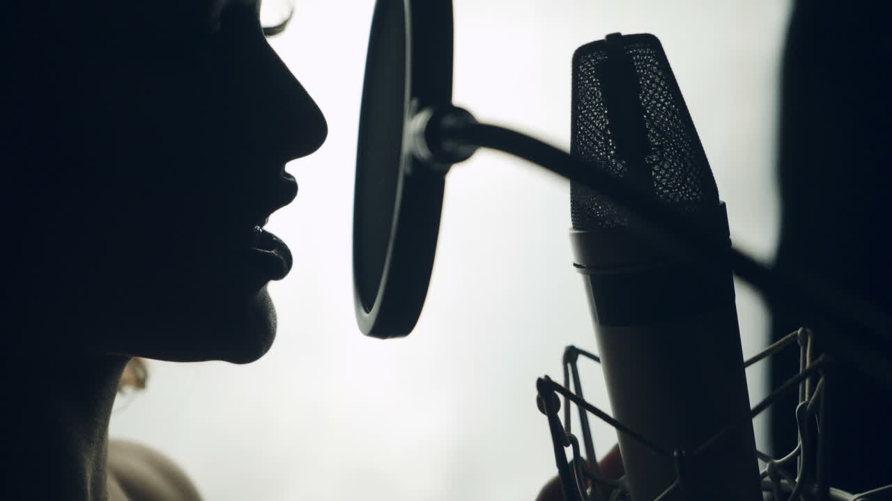 Lovely woman singing into the microphone in the recording studio. Profile of a singer with a beautiful face and lips. Black and white.Close up