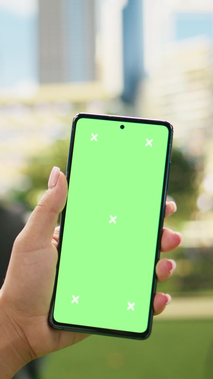 Video verticale: Mockup verticale con schermo verde su telefono tenuto da una donna in abiti casual in un parco cittadino