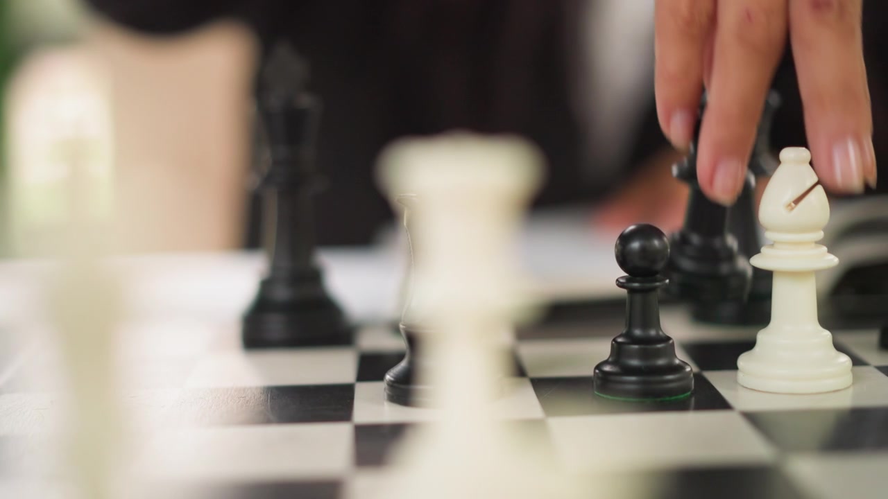 Primo piano della mano di una persona che muove pezzi degli scacchi su una scacchiera, concentrandosi principalmente su pedoni e torri. La scena presenta caselle bianche e nere alternate, con varie posizioni dei pezzi visibili.