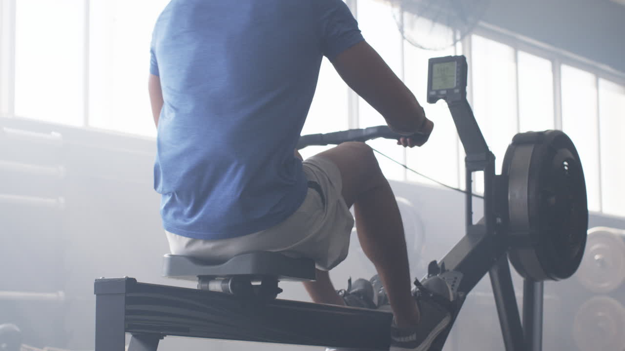 Man exercising on rowing machine in gym, focusing on fitness training
