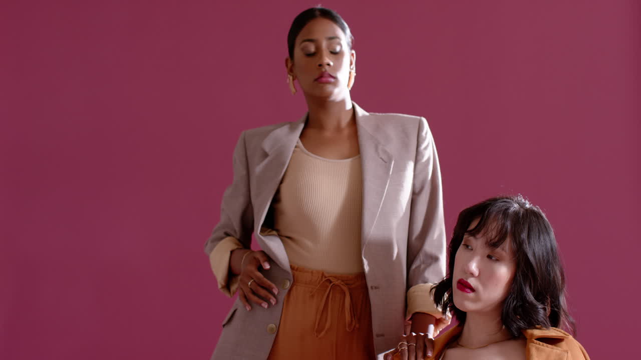 Diverse female colleagues leaning, adjusting blazer and draping trench coat in studio fashion shoot
