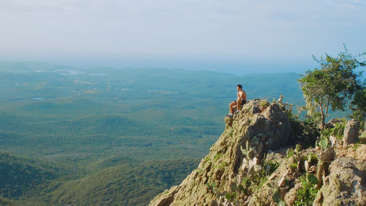 en esta foto puedes ver a un joven sentado al borde del acantilado de la montaña