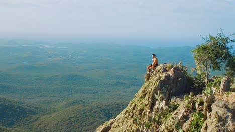 nesta foto você pode ver um jovem homem sentado na beira do penhasco da montanha