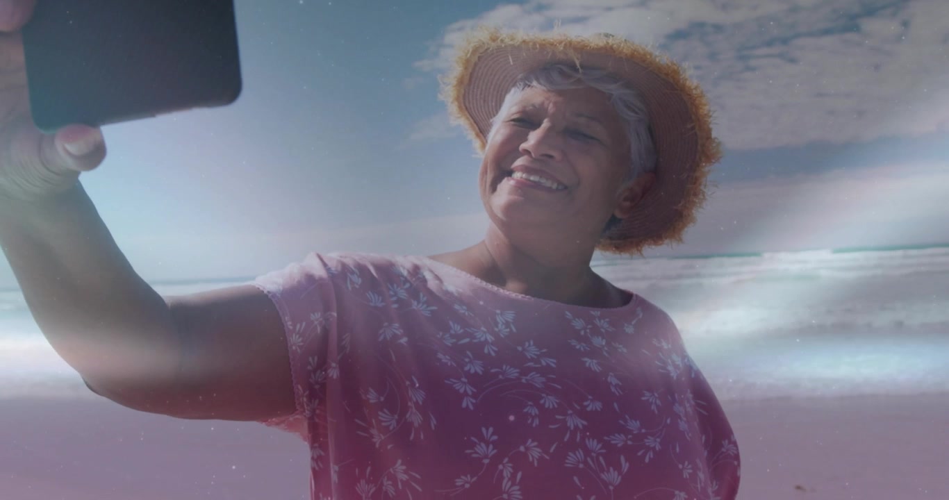 Senior woman arriving at shoreline adjusting phone angle capturing travel selfie with lens flare
