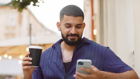 man drinking coffee and using smartphone outside