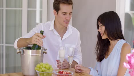 pareja joven sonriente sirviendo champán para beber