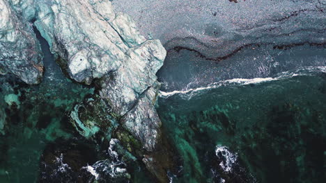 aerial top down pan across rocky white and grey shoreline beach with waves crashing