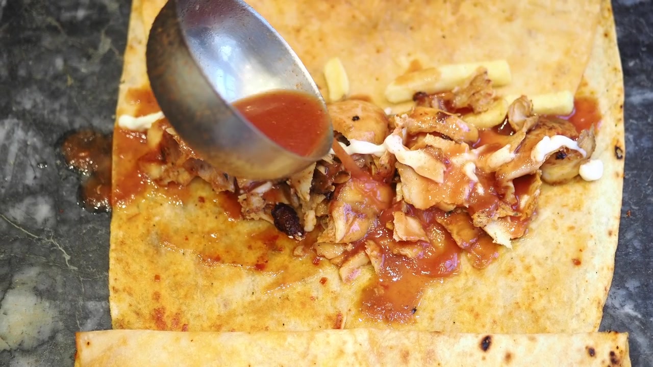 Chef che versa la salsa su un wrap di shawarma di pollo