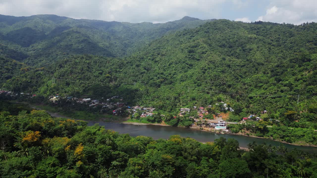dulce muñeca aérea hacia el vecindario en la orilla del río por la montaña tropical verde
