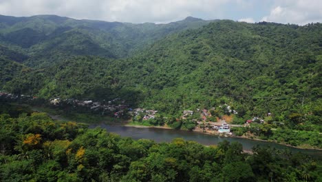 gentle aerial dolly towards neighborhood on river bank by green tropical mountain