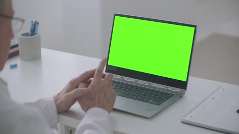 aged doctor is consulting online, laptop with green screen on table, chroma key concept