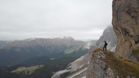 aerial shot from drone passing an young model standing on the edge of a rock overlooking valley in the dolomites, italy