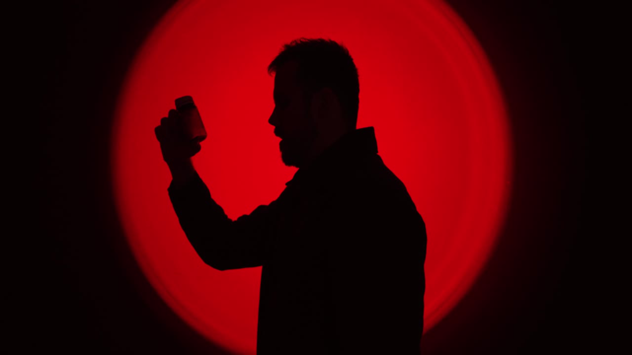 Silhouette cinematografica di profilo laterale di un uomo che tiene in mano uno smartphone su uno sfondo rosso circolare intenso, che suggerisce un uso compulsivo e dipendenza digitale. Ideale per concetti come dipendenza dallo schermo, s