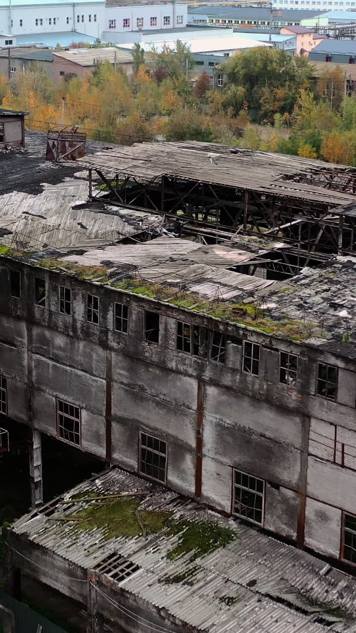 Old abandoned factory. Exterior of ruined buildings with many holes in the roof after military activity. Damaged buildings outdoors. Aerial view. Vertical video