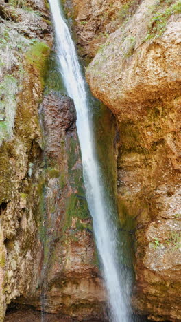 narrow waterfall falling from the sandstones. low angle view at the cataract among the bare rocks. vertical video.