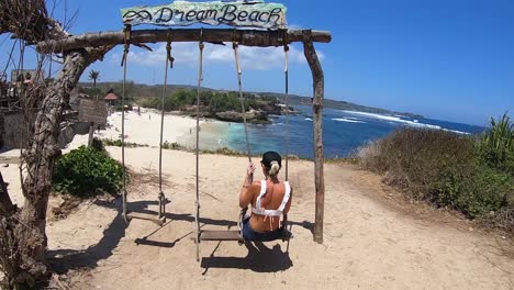 girl on a swing with a beer in her hand on a beach in nusa lembogan, bali, indonesia