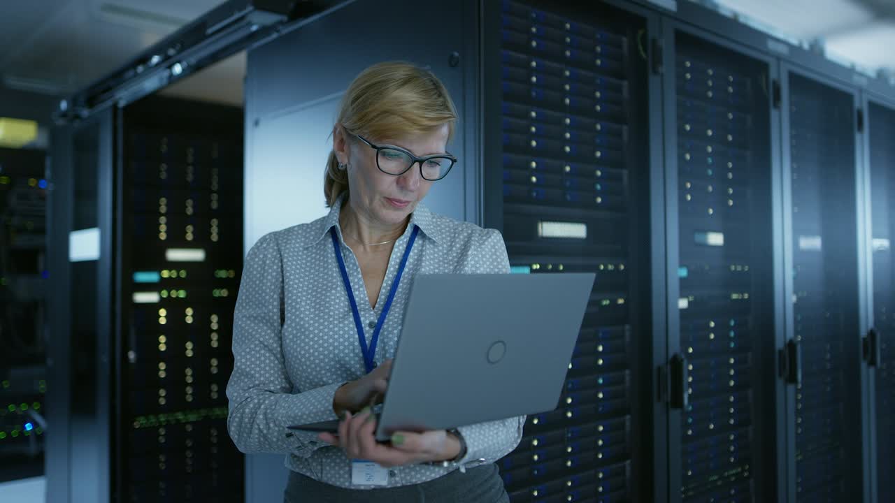 en el centro de datos: técnico informático femenino que ejecuta el programa de mantenimiento en una computadora portátil, controla el funcionamiento óptimo del rack de servidor operativo. centro de datos operativo de telecomunicaciones de alta tecnología moderna.