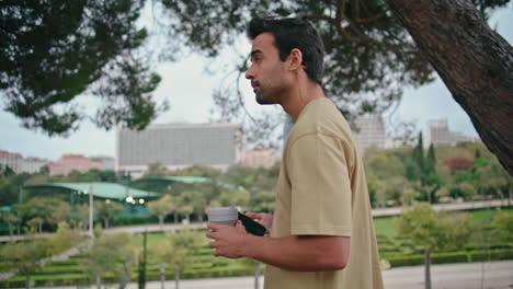 relaxed tourist walking park holding beverage takeaway close up. guy strolling