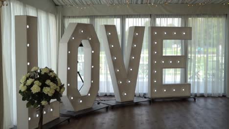 retro lightbox theater style of text love decoration on the backdrop in the wedding reception dinner day party with flowers blurry in foreground, low angle, dolly slider scene