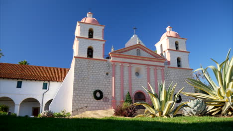 Looking-up-at-the-Santa-Barbara-Spanish-Mission-building-in-California-with-plants-in-a-grassy-field-SLIDE-LEFT