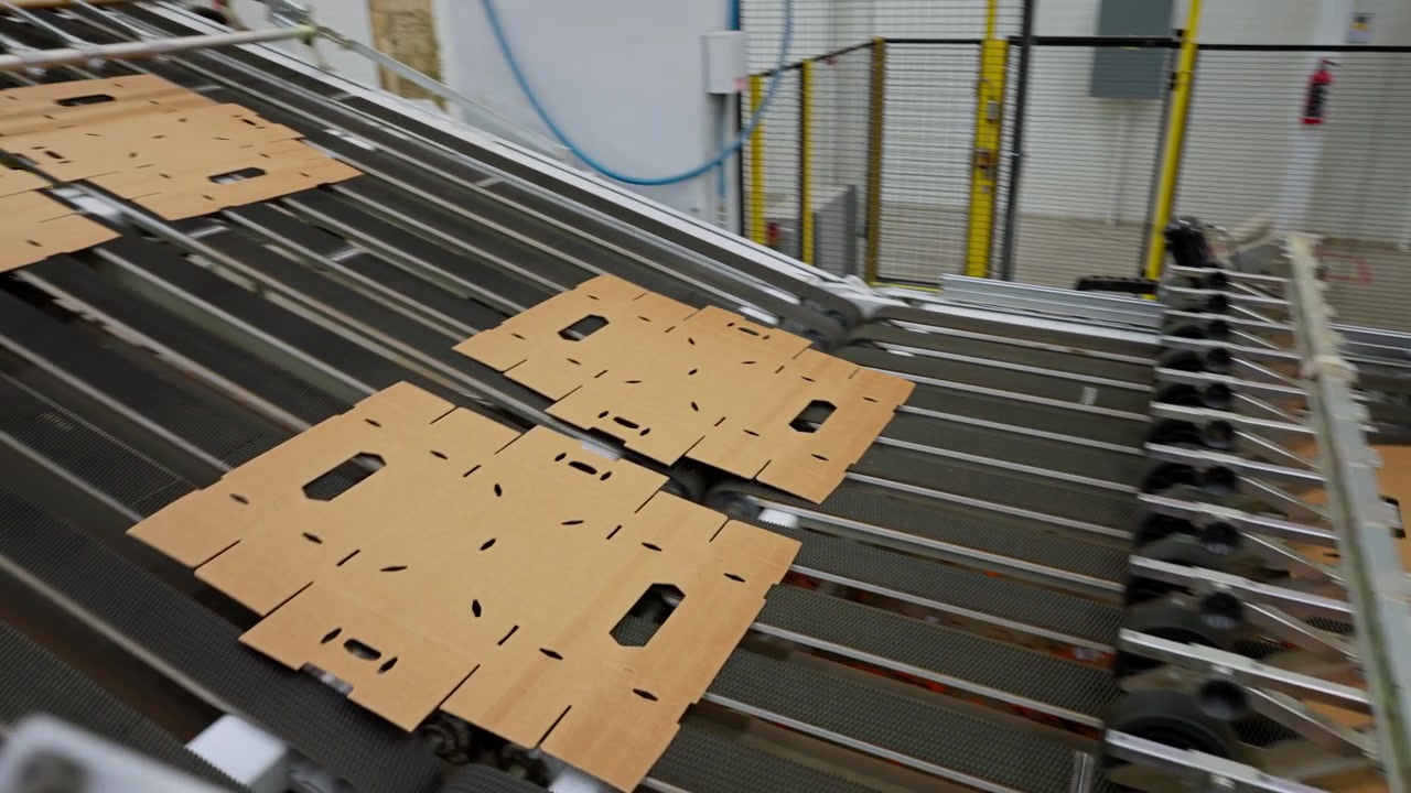 Machines automatisées traitant des feuilles de carton le long d'une ligne de production d'emballages en usine, avec suivi de la découpeuse à rouleaux au trieur-empileur.