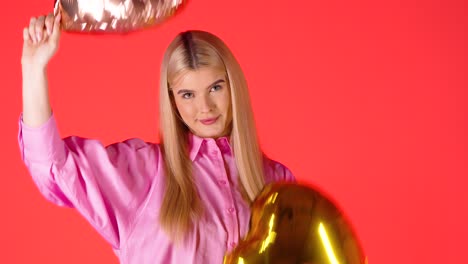 mujer rubia agitando dos globos dorados en forma de corazón, el estado de ánimo de san valentín con fondo de color rojo, toma de estudio