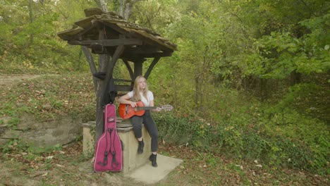 joven feliz mujer rubia músico toca la guitarra bosque deseando bien