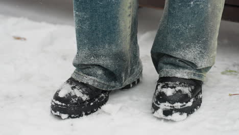 close-up of legs in snow-covered black boots tapping rhythmically on white ground, denim jeans dusted with frost, capturing a wintry moment of subtle movement amidst serene snowy surroundings