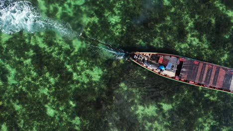 barco de transporte de cola larga flotando lentamente en aguas tranquilas y claras de una laguna poco profunda sobre un hermoso patrón de arrecifes de coral