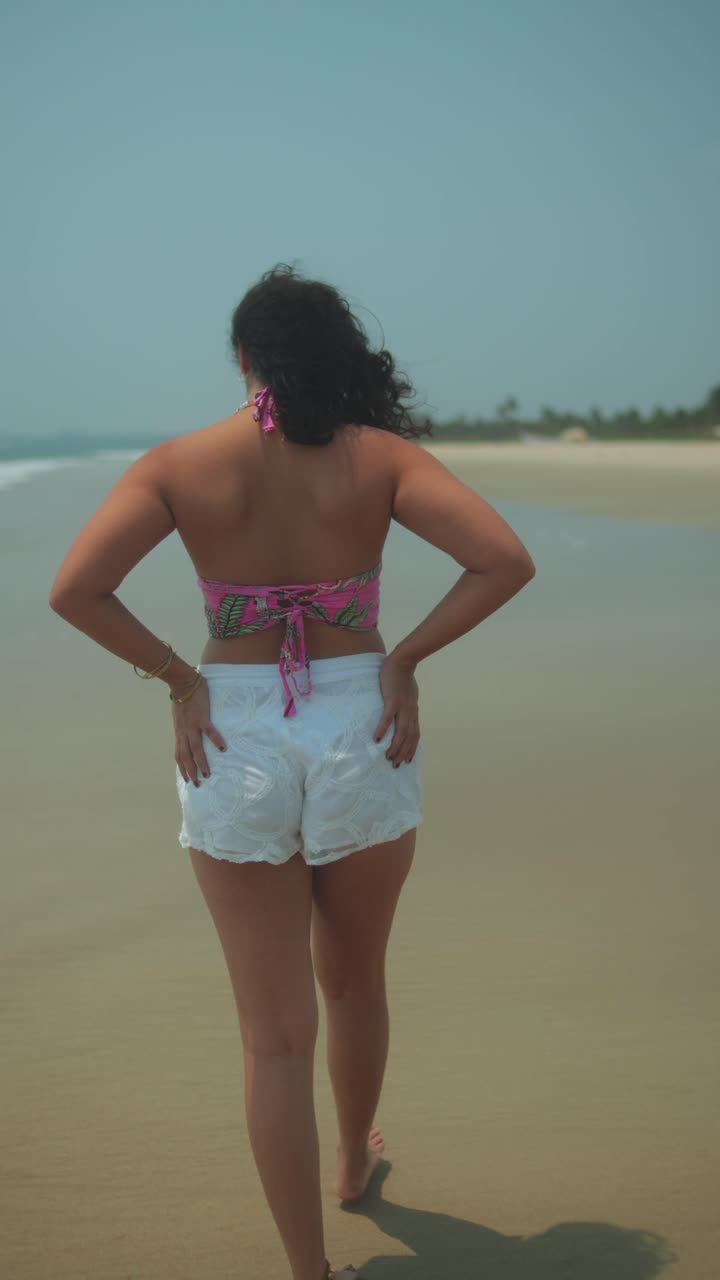 Young woman walking on beach, hair flowing with wind in sunny weather