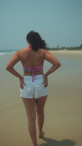 young woman walking on beach, hair flowing with wind in sunny weather