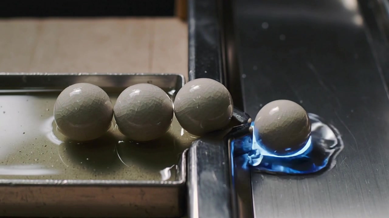Esfera mais à direita se deslocando e rolando da borda metálica para uma abertura iluminada em azul no canal, empurrando a vizinha.